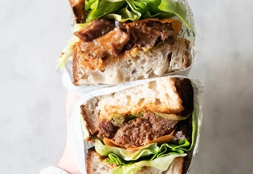A steak sandwich on sourdough with lettuce, wrapped in paper